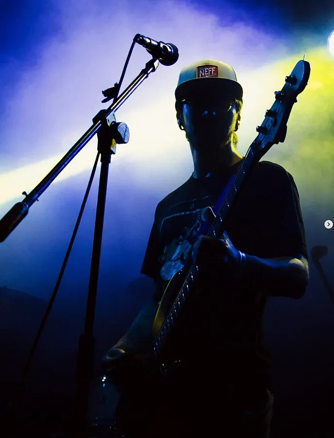Pablo en silueta con el bajo, entre luces azules y amarillas